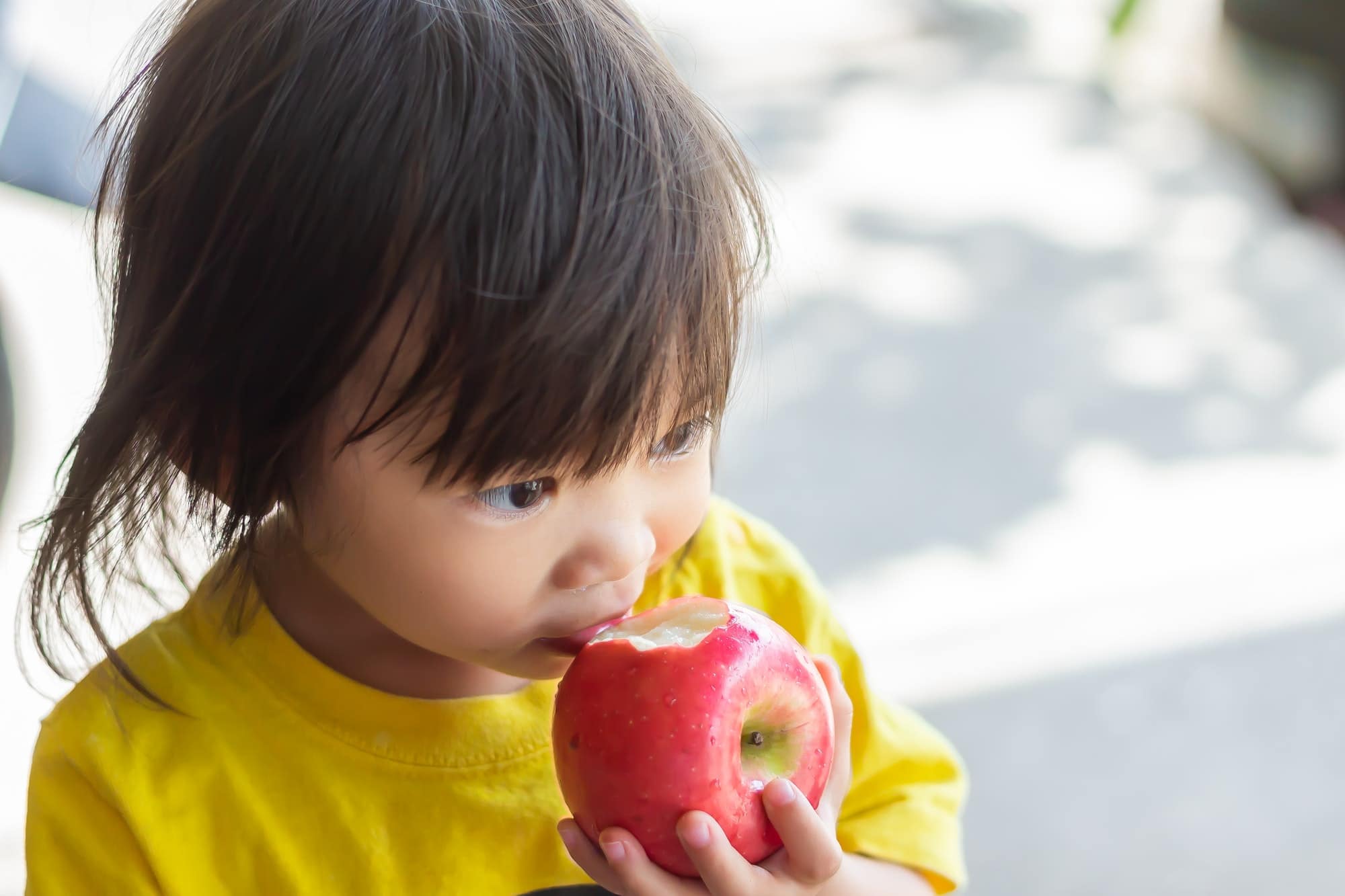 Baby kid child girl eating and biting an apple fruit.